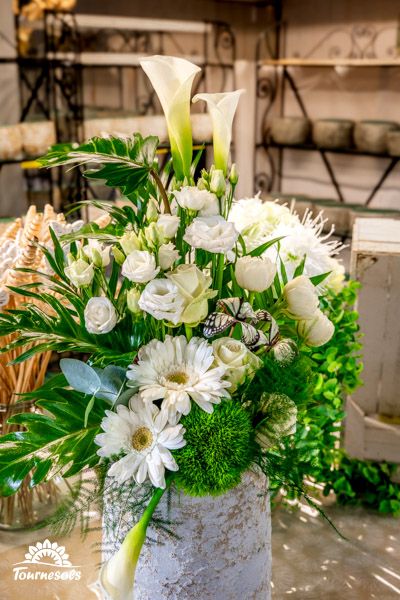 Arrangement floral blanc avec différentes fleurs, feuillage vert dans un vase texturé.